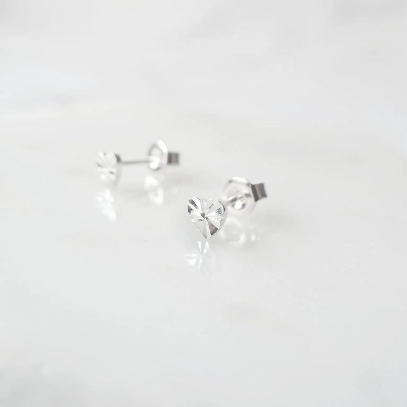 繊細なカットを施したハートモチーフのシルバー925スタッドピアス。光の反射で上品に輝くミニマルデザイン。金属アレルギー対応。
Delicately faceted heart-shaped 925 sterling silver stud earrings with a refined shine. Minimalist design, hypoallergenic.