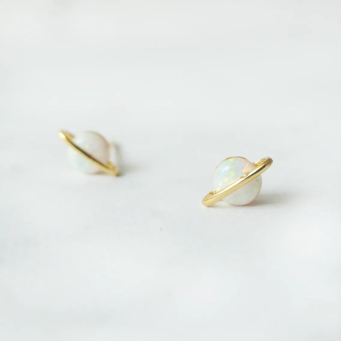 虹色の遊色を放つ天然オパールを18Kゴールドカラーのフレームに包み込んだ、惑星のように幻想的なスタッドピアス。シルバー925に18Kゴールドプレーティングを施し、耳元を柔らかく華やかに彩るデザイン。金属アレルギー対応。