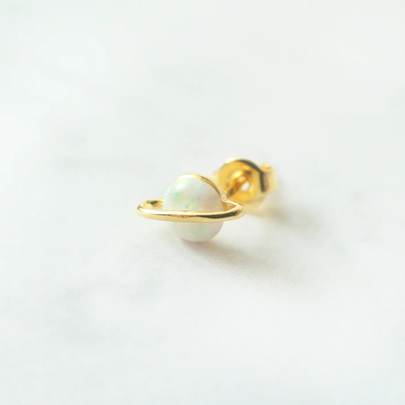 虹色の遊色を放つ天然オパールを18Kゴールドカラーのフレームに包み込んだ、惑星のように幻想的なスタッドピアス。シルバー925に18Kゴールドプレーティングを施し、耳元を柔らかく華やかに彩るデザイン。金属アレルギー対応。