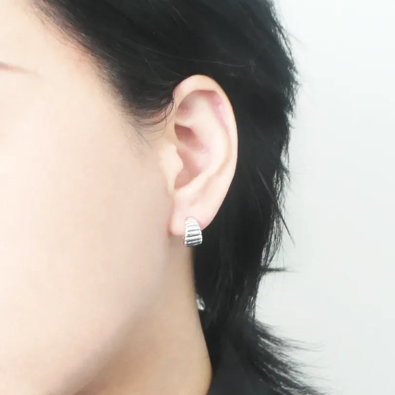 リブデザインのシルバー925ロジウムプレーティングミニフープスタッドピアス。鏡面仕上げで立体感ある輝き、金属アレルギー対応。
Ribbed design mini hoop stud earrings in 925 sterling silver, rhodium plated. Mirror-finish shine with dimensional style, hypoallergenic.