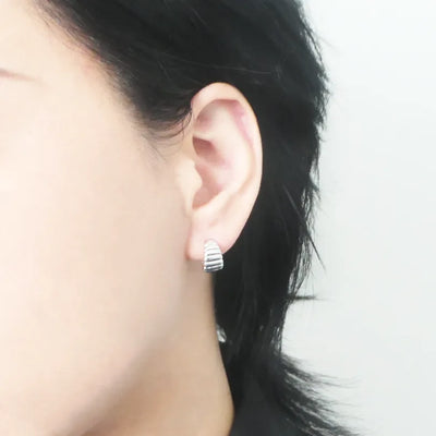 リブデザインのシルバー925ロジウムプレーティングミニフープスタッドピアス。鏡面仕上げで立体感ある輝き、金属アレルギー対応。
Ribbed design mini hoop stud earrings in 925 sterling silver, rhodium plated. Mirror-finish shine with dimensional style, hypoallergenic.
