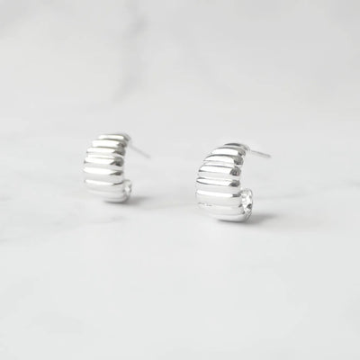 リブデザインのシルバー925ロジウムプレーティングミニフープスタッドピアス。鏡面仕上げで立体感ある輝き、金属アレルギー対応。
Ribbed design mini hoop stud earrings in 925 sterling silver, rhodium plated. Mirror-finish shine with dimensional style, hypoallergenic.
