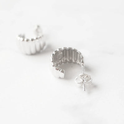 リブデザインのシルバー925ロジウムプレーティングミニフープスタッドピアス。鏡面仕上げで立体感ある輝き、金属アレルギー対応。
Ribbed design mini hoop stud earrings in 925 sterling silver, rhodium plated. Mirror-finish shine with dimensional style, hypoallergenic.