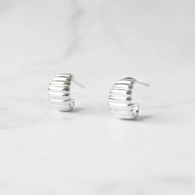 リブデザインのシルバー925ロジウムプレーティングミニフープスタッドピアス。鏡面仕上げで立体感ある輝き、金属アレルギー対応。
Ribbed design mini hoop stud earrings in 925 sterling silver, rhodium plated. Mirror-finish shine with dimensional style, hypoallergenic.