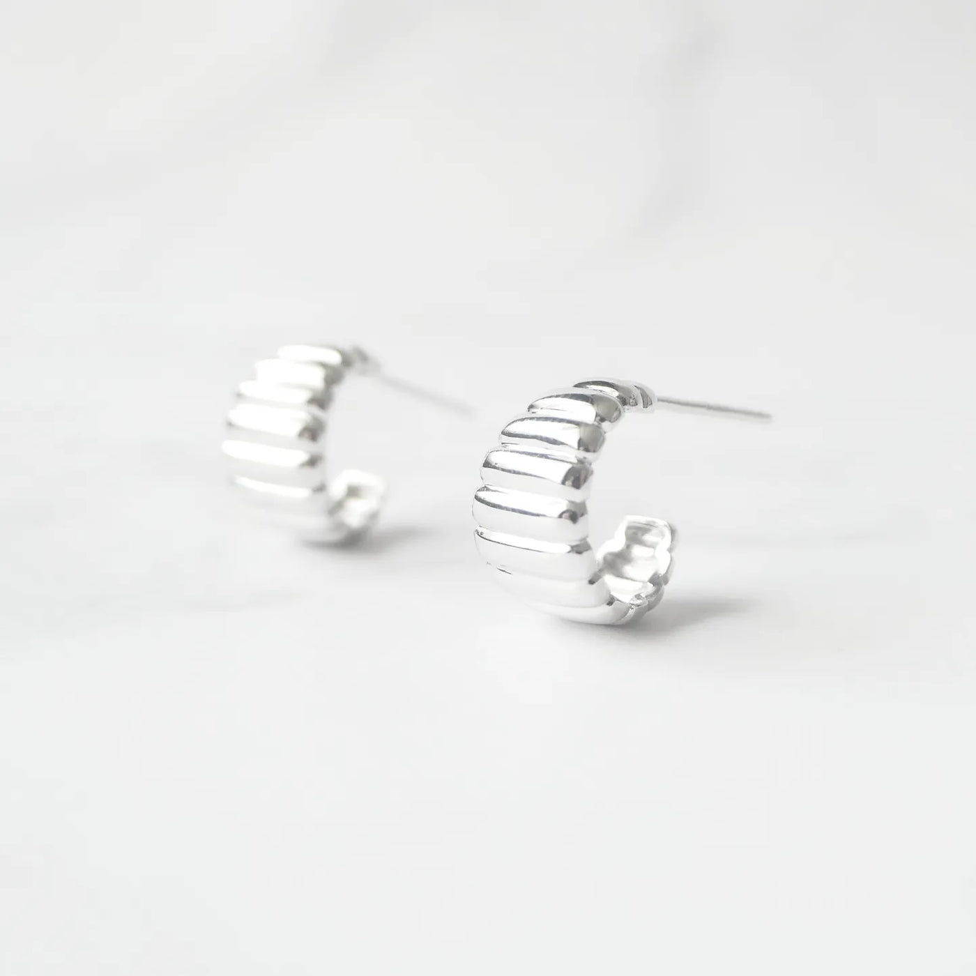 リブデザインのシルバー925ロジウムプレーティングミニフープスタッドピアス。鏡面仕上げで立体感ある輝き、金属アレルギー対応。
Ribbed design mini hoop stud earrings in 925 sterling silver, rhodium plated. Mirror-finish shine with dimensional style, hypoallergenic.