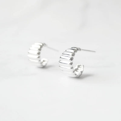 リブデザインのシルバー925ロジウムプレーティングミニフープスタッドピアス。鏡面仕上げで立体感ある輝き、金属アレルギー対応。
Ribbed design mini hoop stud earrings in 925 sterling silver, rhodium plated. Mirror-finish shine with dimensional style, hypoallergenic.