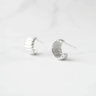 リブデザインのシルバー925ロジウムプレーティングミニフープスタッドピアス。鏡面仕上げで立体感ある輝き、金属アレルギー対応。
Ribbed design mini hoop stud earrings in 925 sterling silver, rhodium plated. Mirror-finish shine with dimensional style, hypoallergenic.