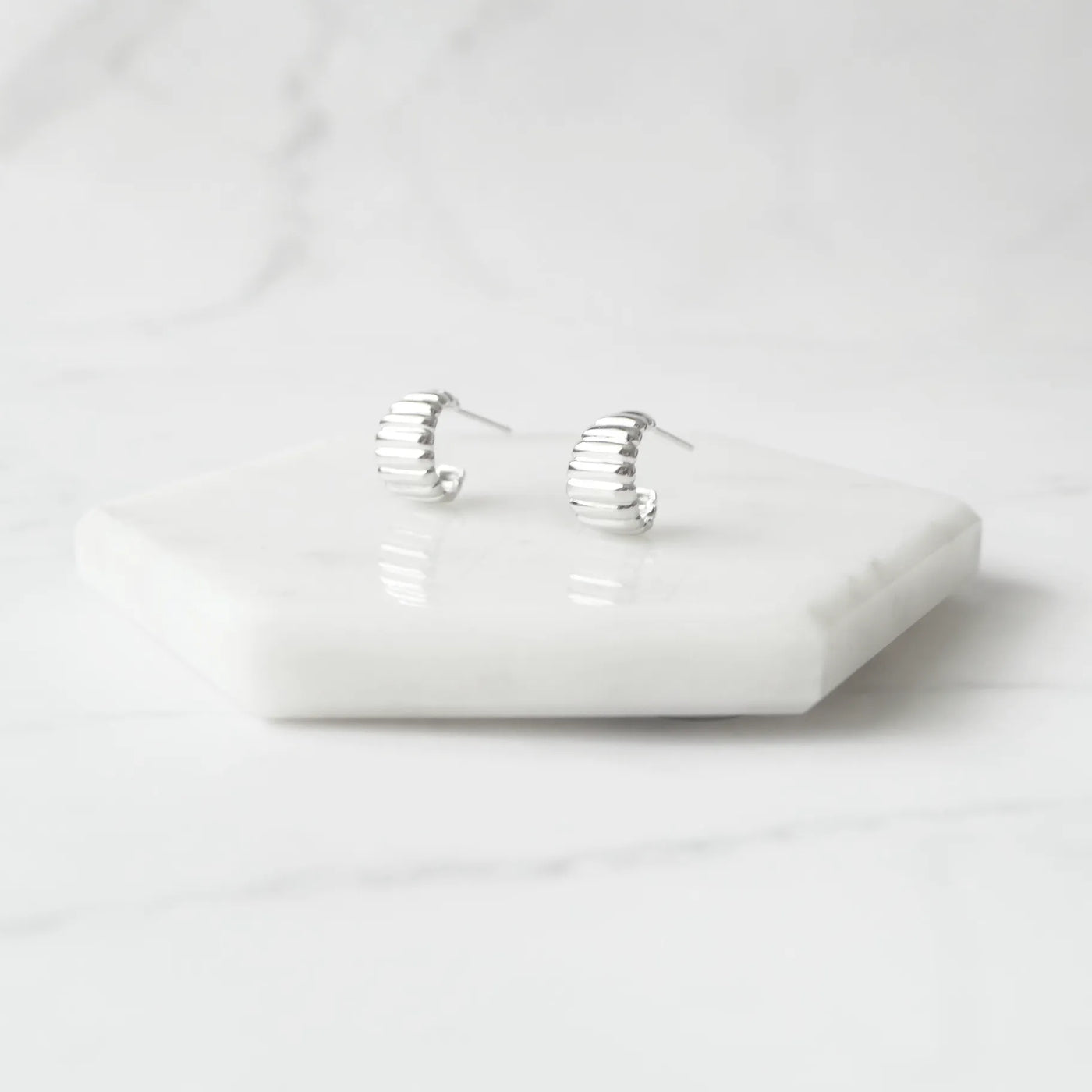 リブデザインのシルバー925ロジウムプレーティングミニフープスタッドピアス。鏡面仕上げで立体感ある輝き、金属アレルギー対応。
Ribbed design mini hoop stud earrings in 925 sterling silver, rhodium plated. Mirror-finish shine with dimensional style, hypoallergenic.