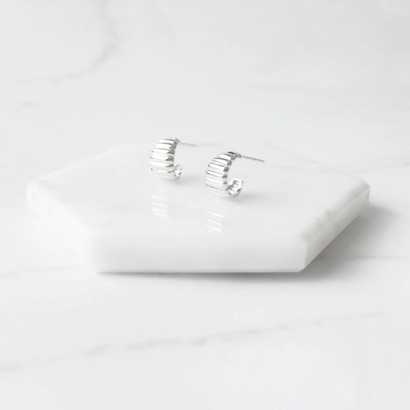 リブデザインのシルバー925ロジウムプレーティングミニフープスタッドピアス。鏡面仕上げで立体感ある輝き、金属アレルギー対応。
Ribbed design mini hoop stud earrings in 925 sterling silver, rhodium plated. Mirror-finish shine with dimensional style, hypoallergenic.