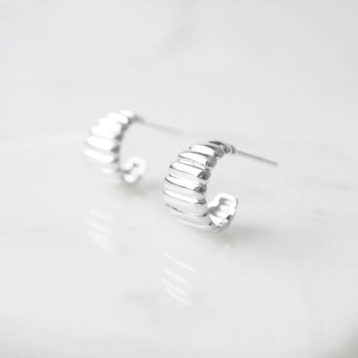 リブデザインのシルバー925ロジウムプレーティングミニフープスタッドピアス。鏡面仕上げで立体感ある輝き、金属アレルギー対応。
Ribbed design mini hoop stud earrings in 925 sterling silver, rhodium plated. Mirror-finish shine with dimensional style, hypoallergenic.