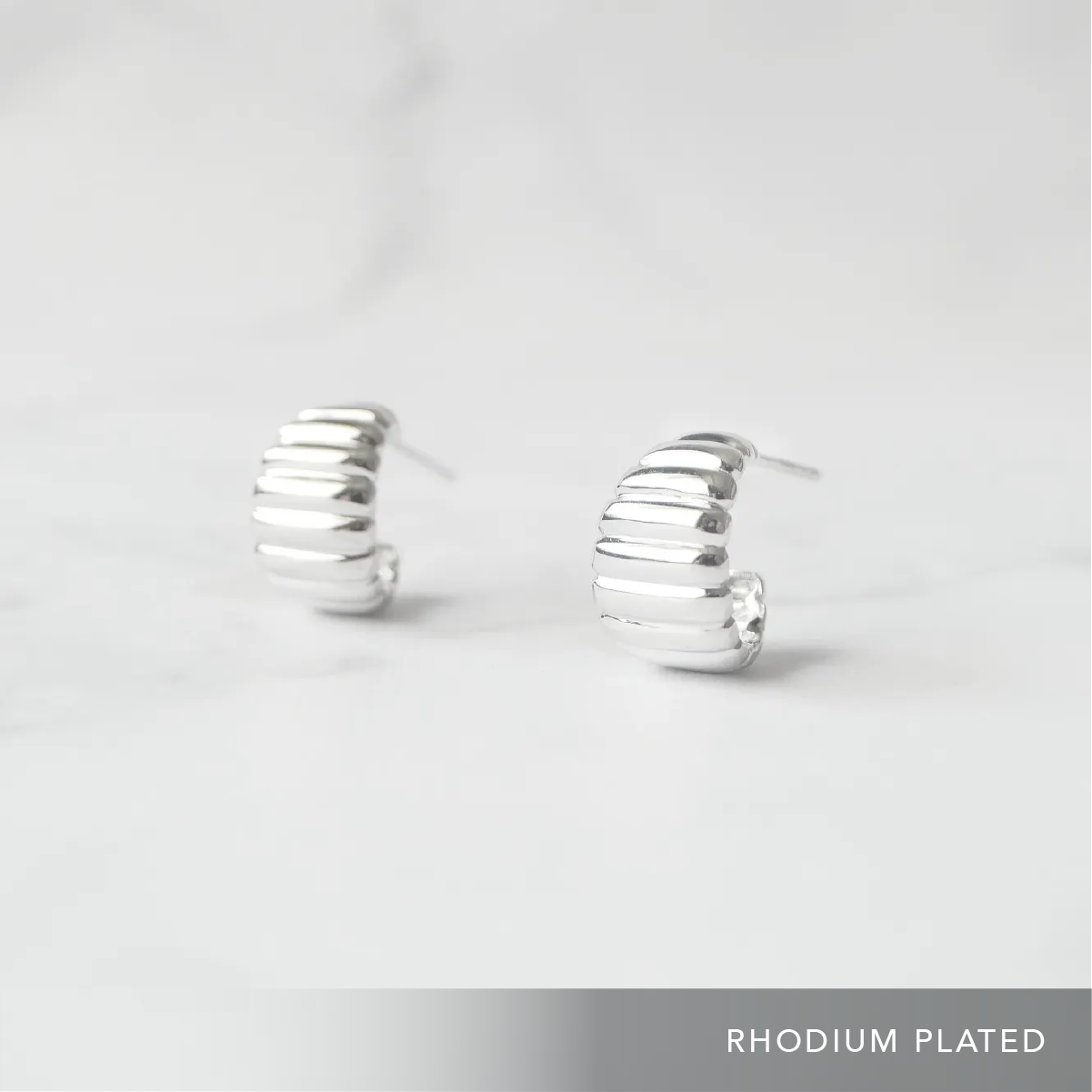 リブデザインのシルバー925ロジウムプレーティングミニフープスタッドピアス。鏡面仕上げで立体感ある輝き、金属アレルギー対応。
Ribbed design mini hoop stud earrings in 925 sterling silver, rhodium plated. Mirror-finish shine with dimensional style, hypoallergenic.