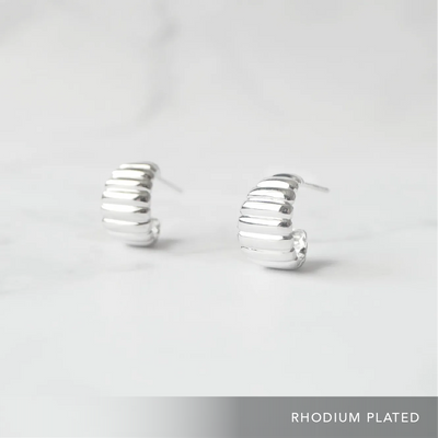 リブデザインのシルバー925ロジウムプレーティングミニフープスタッドピアス。鏡面仕上げで立体感ある輝き、金属アレルギー対応。
Ribbed design mini hoop stud earrings in 925 sterling silver, rhodium plated. Mirror-finish shine with dimensional style, hypoallergenic.