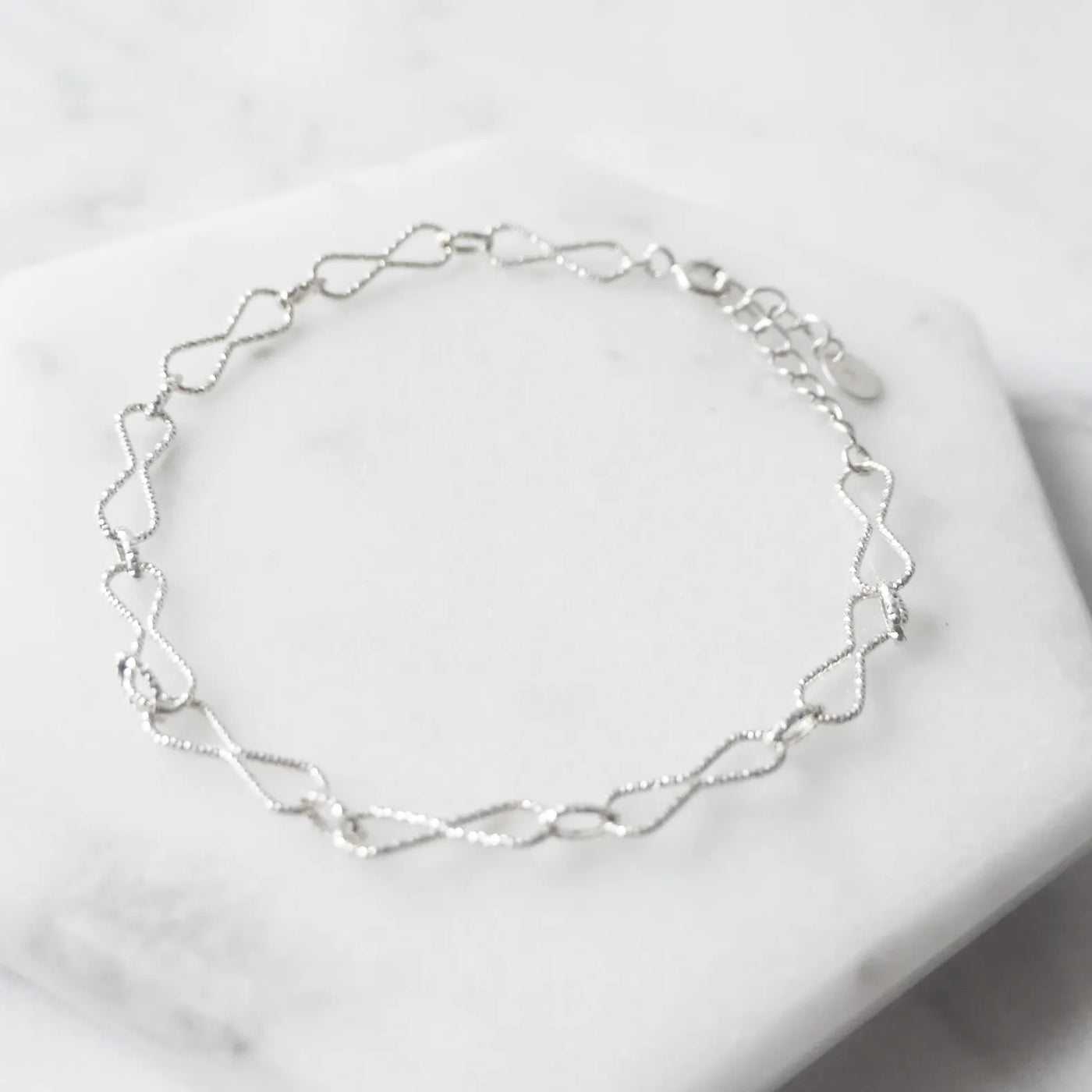 くり抜きのリボンモチーフと刻み模様が施されたチェーンブレスレット。シルバー925素材・金属アレルギー対応。