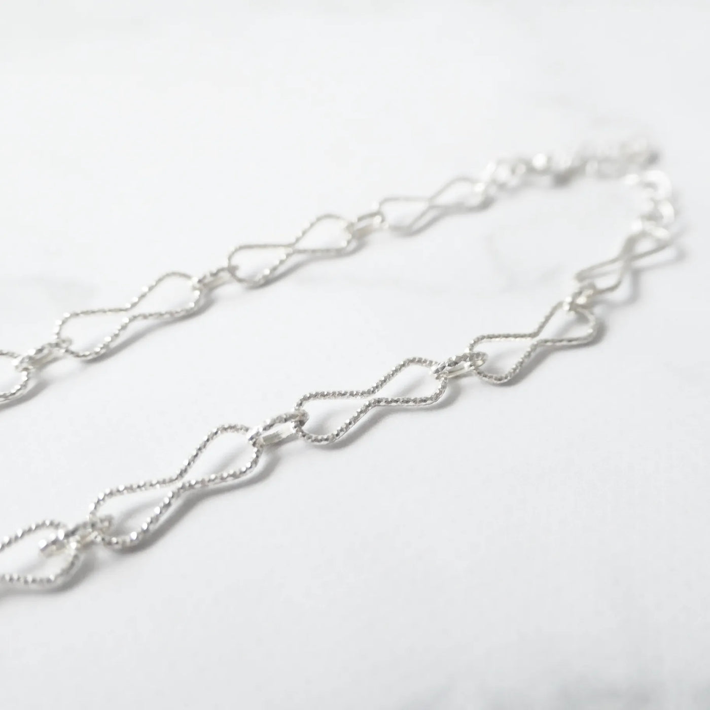 くり抜きのリボンモチーフと刻み模様が施されたチェーンブレスレット。シルバー925素材・金属アレルギー対応。