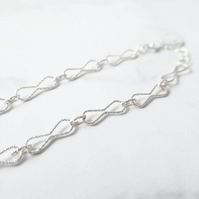 くり抜きのリボンモチーフと刻み模様が施されたチェーンブレスレット。シルバー925素材・金属アレルギー対応。