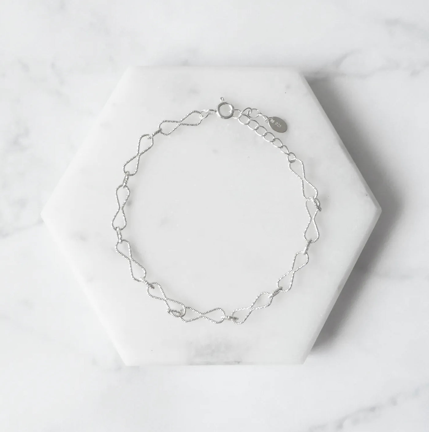 くり抜きのリボンモチーフと刻み模様が施されたチェーンブレスレット。シルバー925素材・金属アレルギー対応。