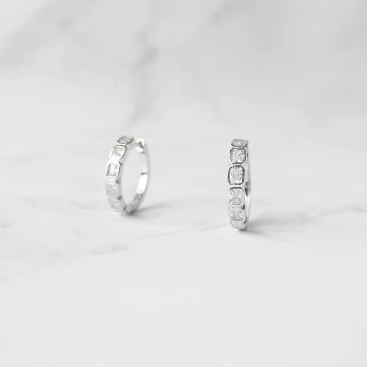 スクエアカットのジルコニアを並べたシルバー925ロジウムプレーティングフープピアス。モダンで上品な輝き、金属アレルギー対応。
Hoop earrings with square-cut zirconia in 925 sterling silver, rhodium plated. Modern, elegant sparkle, hypoallergenic.