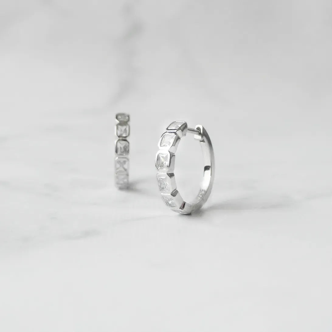 スクエアカットのジルコニアを並べたシルバー925ロジウムプレーティングフープピアス。モダンで上品な輝き、金属アレルギー対応。
Hoop earrings with square-cut zirconia in 925 sterling silver, rhodium plated. Modern, elegant sparkle, hypoallergenic.