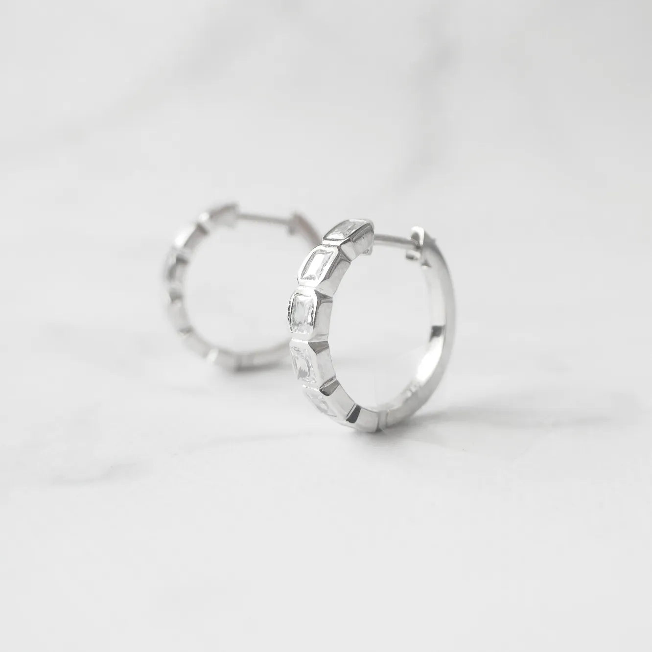スクエアカットのジルコニアを並べたシルバー925ロジウムプレーティングフープピアス。モダンで上品な輝き、金属アレルギー対応。
Hoop earrings with square-cut zirconia in 925 sterling silver, rhodium plated. Modern, elegant sparkle, hypoallergenic.