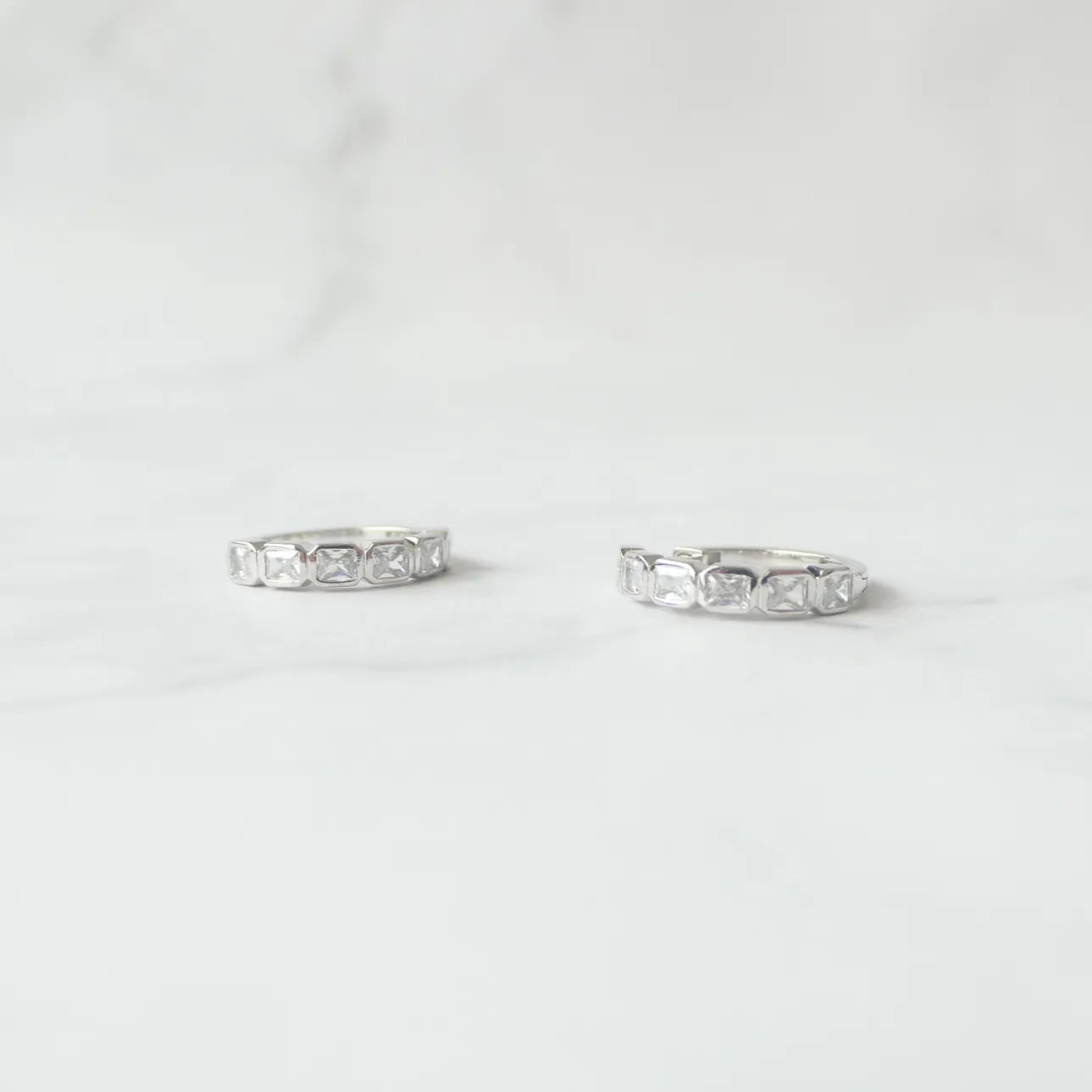スクエアカットのジルコニアを並べたシルバー925ロジウムプレーティングフープピアス。モダンで上品な輝き、金属アレルギー対応。
Hoop earrings with square-cut zirconia in 925 sterling silver, rhodium plated. Modern, elegant sparkle, hypoallergenic.