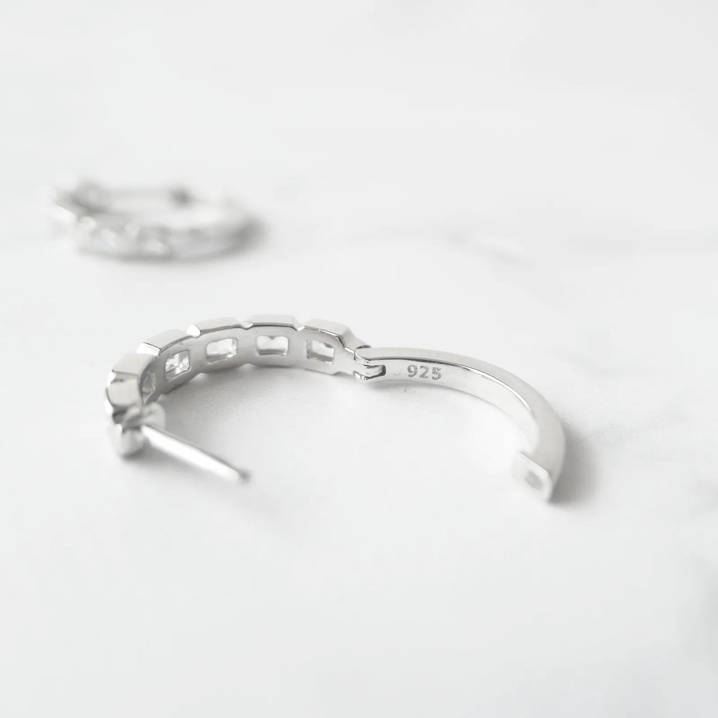 スクエアカットのジルコニアを並べたシルバー925ロジウムプレーティングフープピアス。モダンで上品な輝き、金属アレルギー対応。
Hoop earrings with square-cut zirconia in 925 sterling silver, rhodium plated. Modern, elegant sparkle, hypoallergenic.