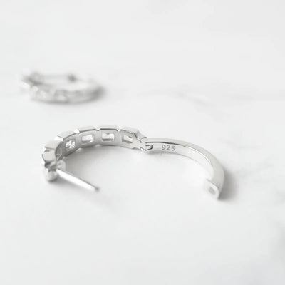 スクエアカットのジルコニアを並べたシルバー925ロジウムプレーティングフープピアス。モダンで上品な輝き、金属アレルギー対応。
Hoop earrings with square-cut zirconia in 925 sterling silver, rhodium plated. Modern, elegant sparkle, hypoallergenic.