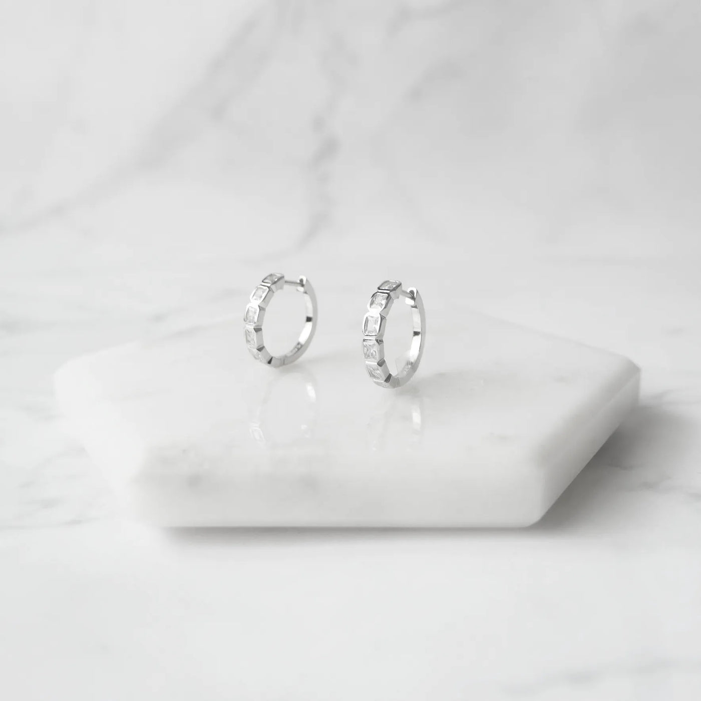スクエアカットのジルコニアを並べたシルバー925ロジウムプレーティングフープピアス。モダンで上品な輝き、金属アレルギー対応。
Hoop earrings with square-cut zirconia in 925 sterling silver, rhodium plated. Modern, elegant sparkle, hypoallergenic.