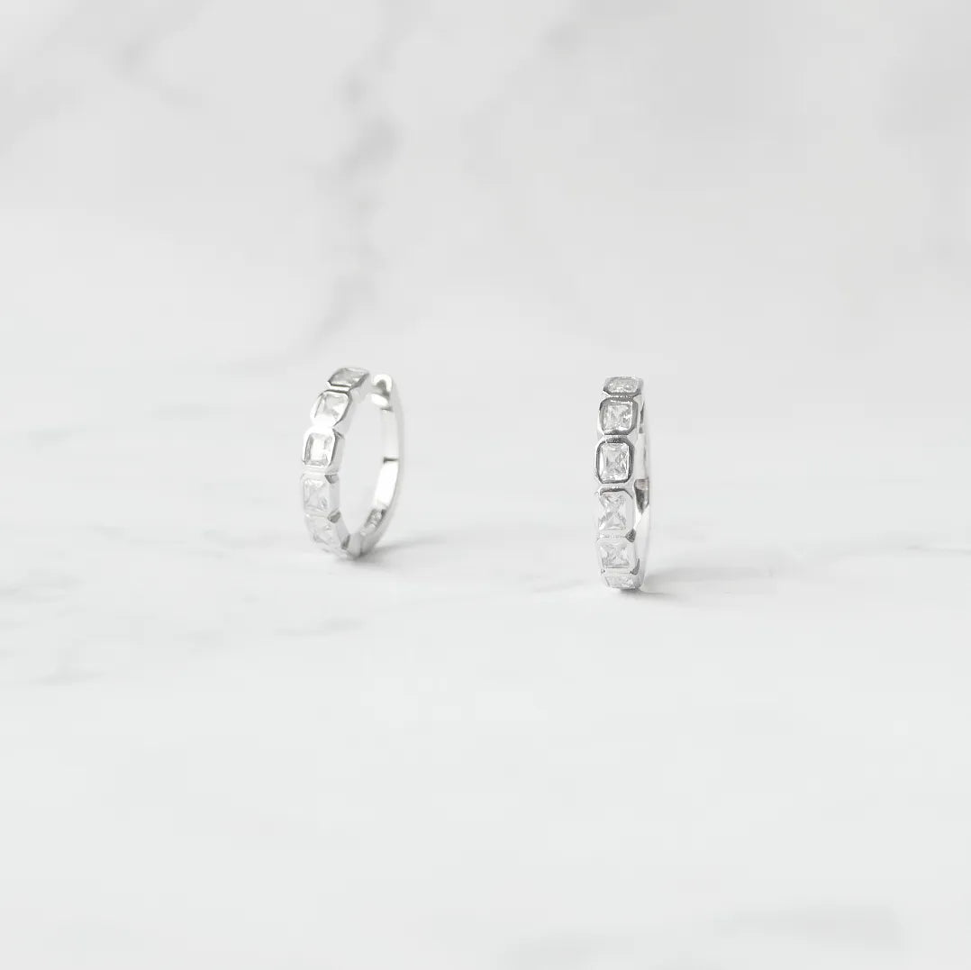 スクエアカットのジルコニアを並べたシルバー925ロジウムプレーティングフープピアス。モダンで上品な輝き、金属アレルギー対応。
Hoop earrings with square-cut zirconia in 925 sterling silver, rhodium plated. Modern, elegant sparkle, hypoallergenic.