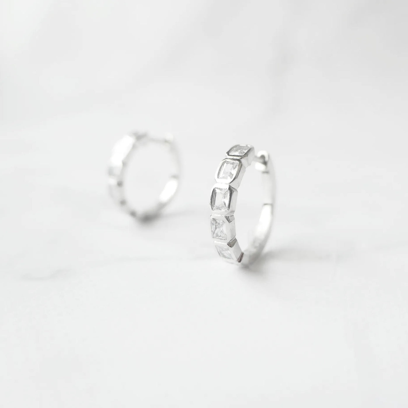 スクエアカットのジルコニアを並べたシルバー925ロジウムプレーティングフープピアス。モダンで上品な輝き、金属アレルギー対応。
Hoop earrings with square-cut zirconia in 925 sterling silver, rhodium plated. Modern, elegant sparkle, hypoallergenic.